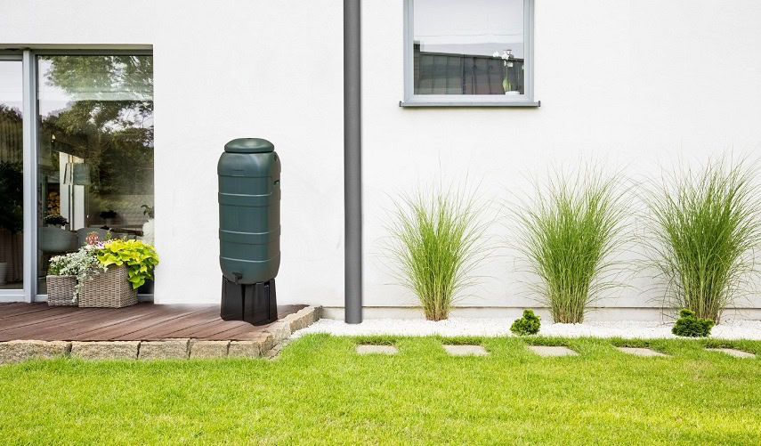 100 liter regenton op verhoogstuk tegen witte huis met planten